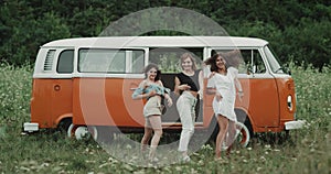 Three pretty ladies dancing choreography in front of a retro van in the middle of nature. 4k