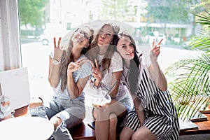 Three pretty slim girls with long dark hair,wearing casual style,sit on the windowsill in a modern coffee shop.