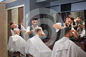 Three professional barbers trimming, cutting and styling male clients` hair. photo