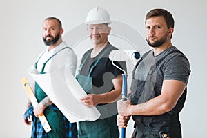 Three professional builder with painting roll and renovation plans standing in empty interior