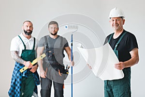 Three professional builder with painting roll and renovation plans standing in empty interior