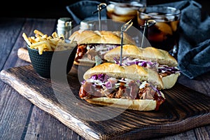 Three pulled pork sliders on a wooden board served with french fries and two cola beverages in behind.