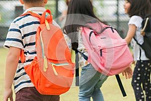 Three pupils of primary school go hand in hand. Boy and girl with school bags behind the back. Beginning of school lessons.