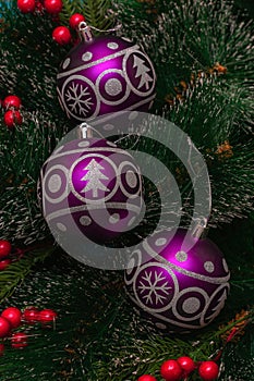 Three purple festive balloons with the image of a Christmas tree and snowflakes hanging on artificial branches of a spruce