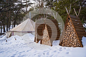 Three pyramidal sheds filled with dry wood in the middle of a snowy forest