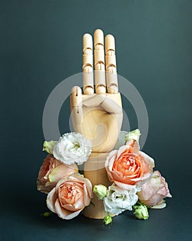 Three raised fingers of wooden hand with flowers on dark green background
