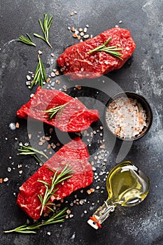 Three Raw beef steak with spices  onions and rosemary on dark slate or concrete background. Top view