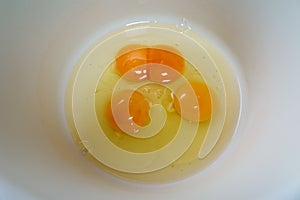 Three raw eggs with double yolk in one, in a white bowl, top view