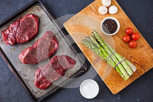 Three raw filet steaks with green asparagus