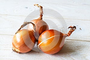 Three raw fresh yellow onions on a wooden rustic table. Vegetables, vegetarian and healthy eating. Food ingredients