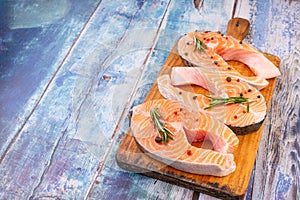 Three raw salmon steaks on a wooden cutting board prepared for cooking, top view