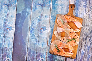 Three raw salmon steaks on a wooden cutting board prepared for cooking, top view