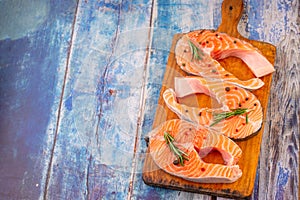 Three raw salmon steaks on a wooden cutting board prepared for cooking, top view