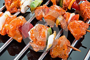 Three raw shaslik skewers on a cooking grate with reflections on