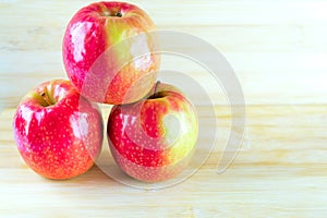 Three red apples on wooden table.