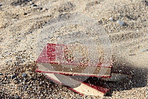 Three red books on the sand, covered with sand, concept of transience of time, blurred background.