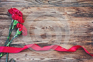 three red carnations, scarlet silk ribbon, on wooden table