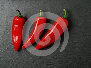 Three red chilly peppers on a dark slate plate, Top view
