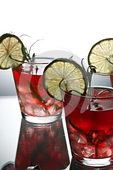 Three red cocktails with lime and rosemary standing on glass in studio, gray background