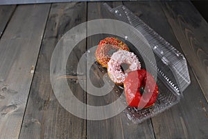 Three red donuts in a plastic box on a gray background with space for copyspace text. Donut Day Candy Delivery American Food