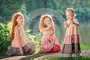 Three red-haired sisters in long linen dresses blow bubbles in the park on sunny summer day
