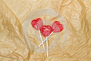 Three red heart shaped lollipops on a wrinkled brown paper