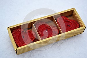 Three red hearts in a cortonal box - candles on white snow