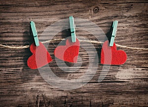 Three red hearts hanging on a cord on a wooden background