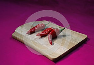 Three red hot peppers on board in still life, diagonal view, with magenta background