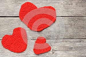 Three red knitted hearts on a gray wooden background, symbolizing love and family