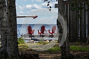 Three red muskoka chairs on a dock looking out into the lake