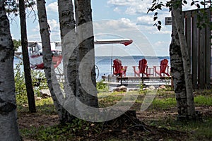 Three red muskoka chairs on a dock looking out to the lake and an airplane docked be