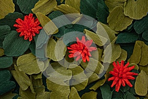 Three red paper flowers among green leaves, origami