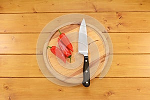 Three red peppers with a knife on a chopping board