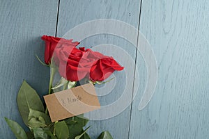 Three red roses on blue wood table with 8 march paper card