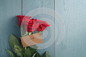 Three red roses on blue wood table with 8 march paper card