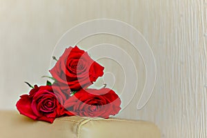 Three red roses lying on a beige background. The focus on the near rose. Close-up. Copy space