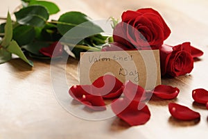 Three red roses with petals on wood table and paper card for valentines day