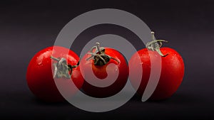 Three red small juicy cherry tomatoes on a black background close-up