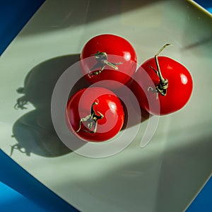 Three red tomatoes lie on a plate in the sunlight
