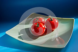 Three red tomatoes lie on a plate in the sunlight