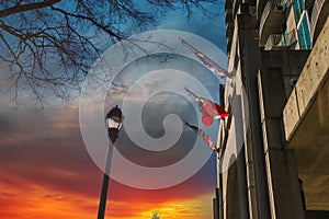 Three red, white and blue flags flying on a concrete hotel with a tall black light posts and red sky and powerful clouds