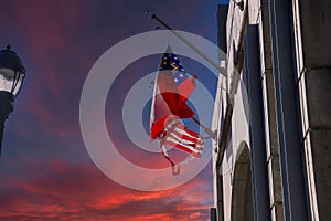 Three red, white and blue flags flying on a concrete hotel with a tall black light posts and red sky and powerful clouds