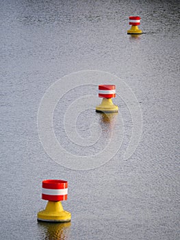 Three red-yellow-white buoys drifting on a river