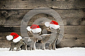 Three reindeer wearing santa hats on brown wooden background.