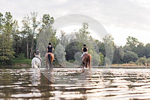 Three rider girls crossing the river riding their horses