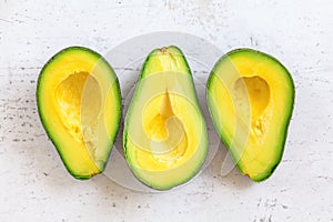 Three ripe avocado halves with bright yellow pulp on white working board, tabletop view