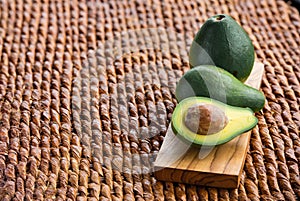 Three ripe avocados on wooden background: two whole and one cut.