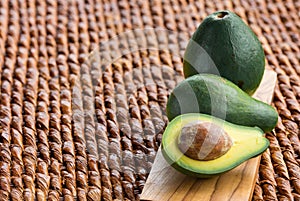 Three ripe avocados on wooden background: two whole and one cut.