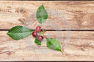 Three ripe berries of a red cherry on wooden boards background. Sweet cherry with green leaves on a rough wood. Minimalist image